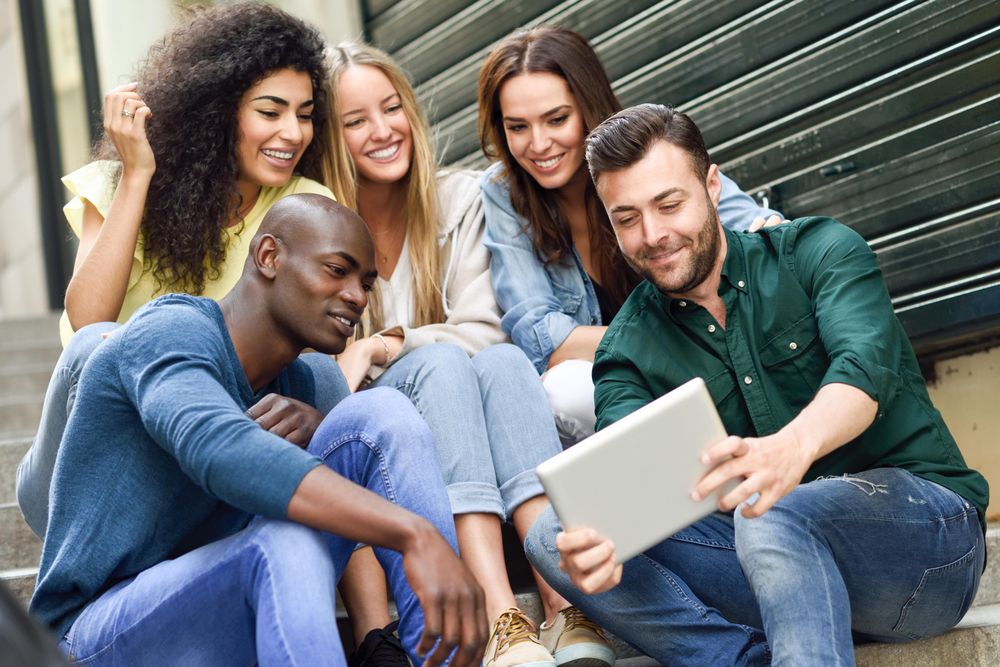Men and women enjoying something on digital tablet while sitting on outdoor cement staircase