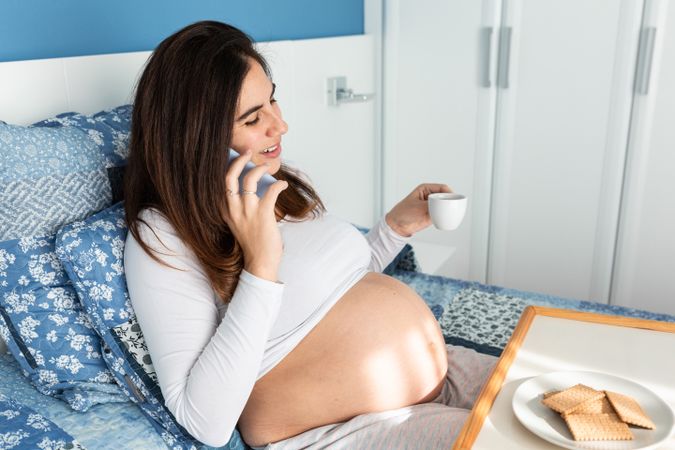 Pregnant woman having breakfast and talking on smartphone