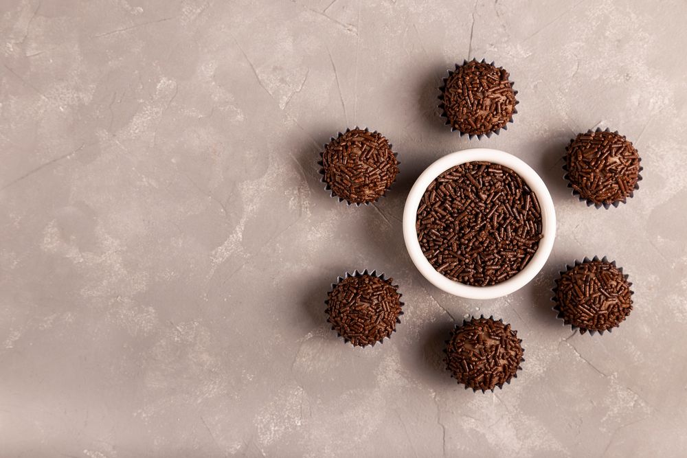 Top view of chocolate truffles arranged around bowl of sprinkles on marble surface with space for text