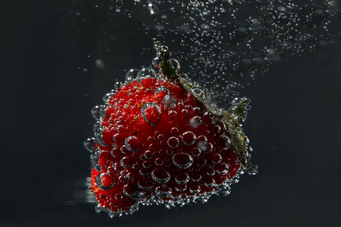 Side view of sparkling water on dark background with a floating strawberry