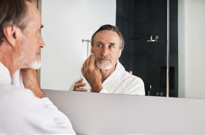Older man cleaning his face in bathroom mirror