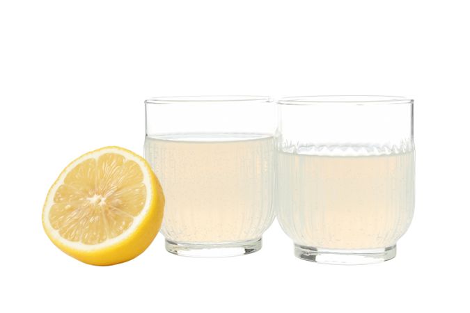 Half of lemon and glasses with limoncello, isolated on light background