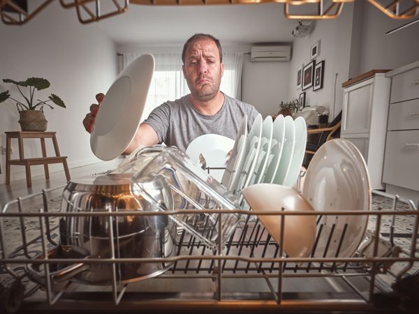 Puzzled man unloading dishwasher in kitchen
