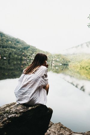 Woman sitting on rock near lake and mountains