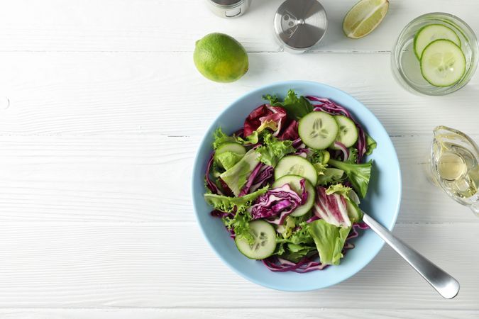 Plate with fresh salad, spices and oil on wooden background, top view