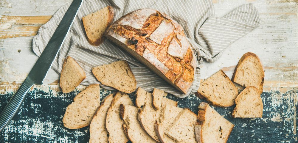 Homemade loaf, with slices arranged in line with serrated knife, on wooden board, wide composition