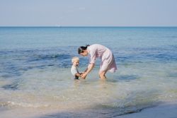 Woman and small kid having fun with water while relaxing on seacoast at resort