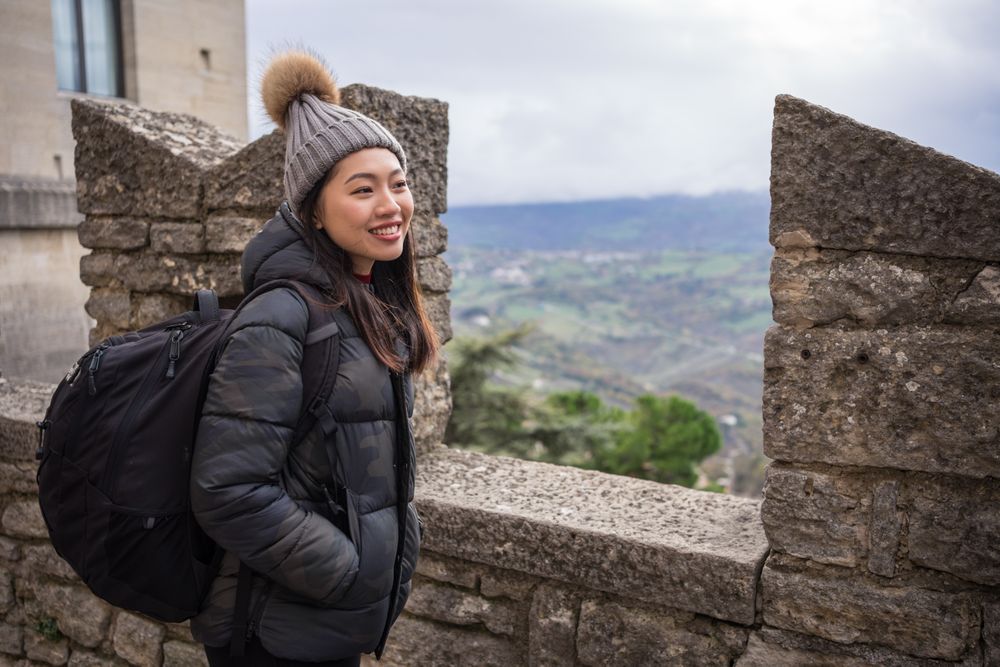 Relaxed Asian woman in warm hat with pompom sightseeing and looking at city down