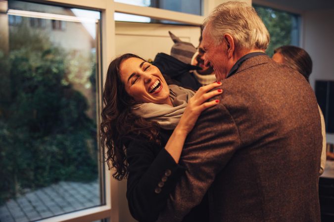 Older father and daughter greeting each other at front door for holiday celebration