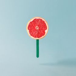 Grapefruit half with ice cream stick on pastel blue background