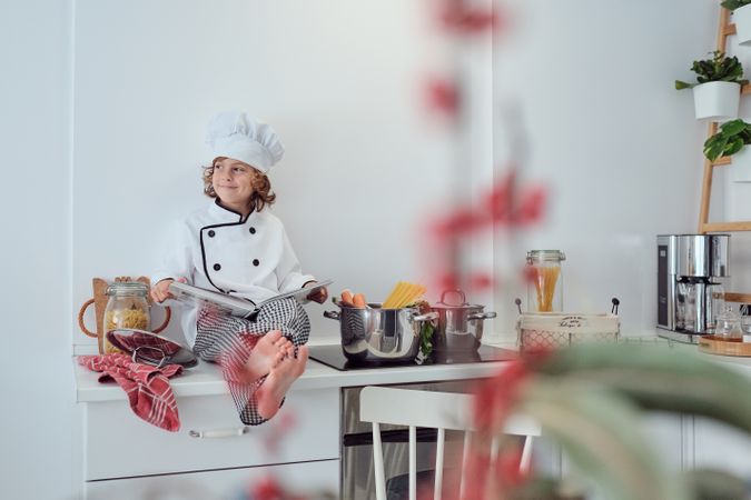 Dreamy preteen boy in chef uniform sitting scrolling cookbook