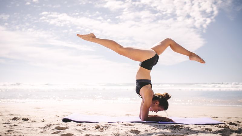 Fitness woman doing handstand yoga asana on the beach