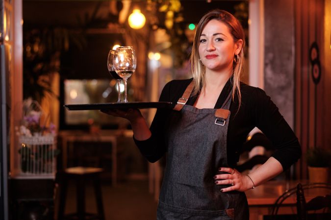 Cheerful waitress holding tray with wineglasses