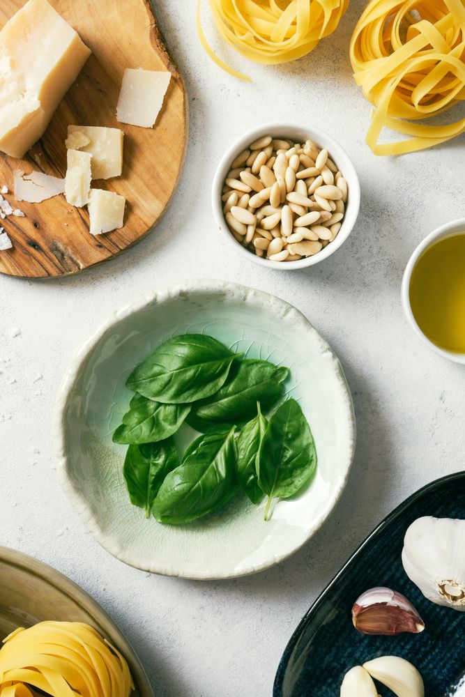 Basil leaves and ingredients for pesto sauce on plates on table