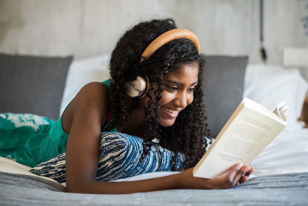 Black teenage reading a book on bed