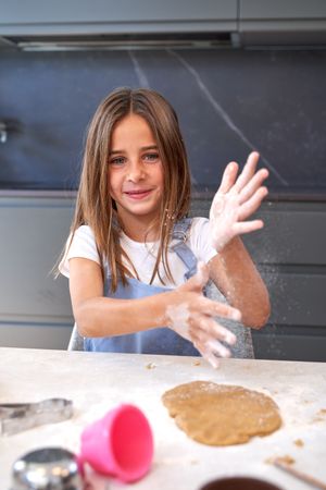Happy cute child slapping hands above dough in kitchen