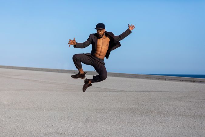 Black man jumping high and clicking heels with open shirt outside