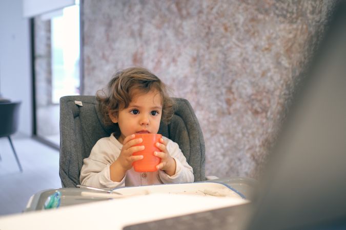Cute baby drinking hot beverage at home