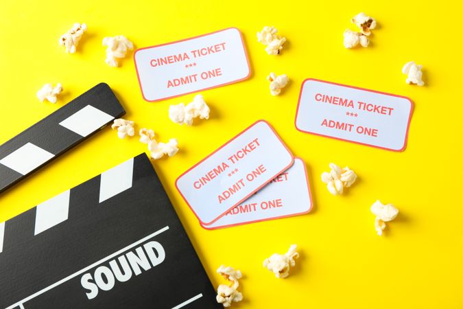 Flat lay composition with clapperboard, popcorn and tickets on yellow background