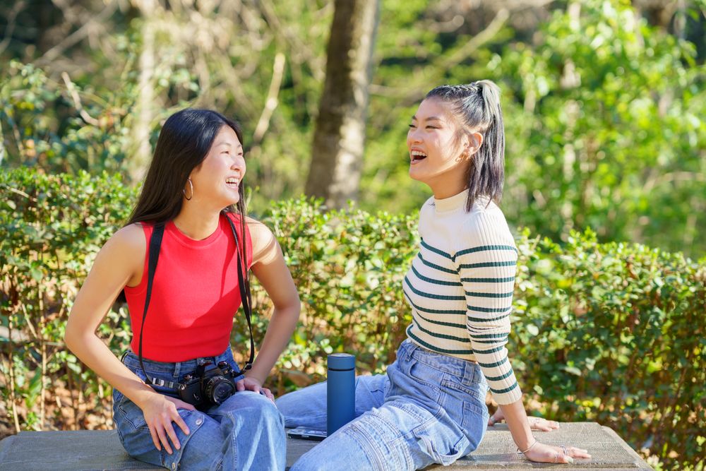 Two women sitting facing each other on outdoor bench in beautiful green park
