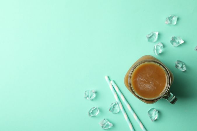 Jar of ice coffee, ice cubes and straws on mint background