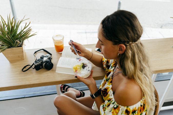 Stylish woman eating and reading book in cafe