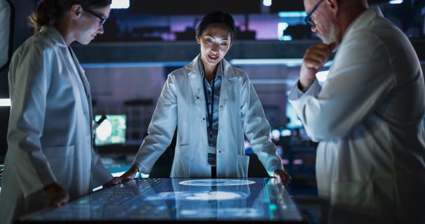 Modern Hospital Medical Research Center: Diverse Colleagues Gathered Around Interactive Touch Screen Table With MRI Scans Of Brain On Display.
