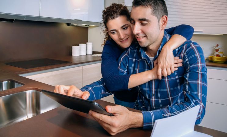 Woman holding man as they do admin work together in their kitchen