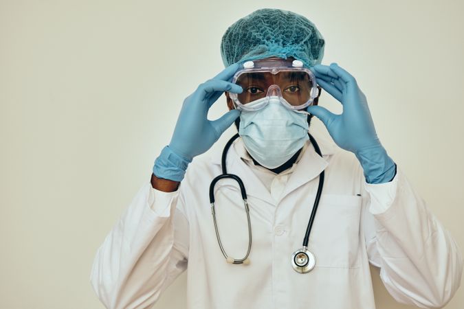 Portrait of Black male doctor in bright studio with ppe gear ready for surgery removing googles