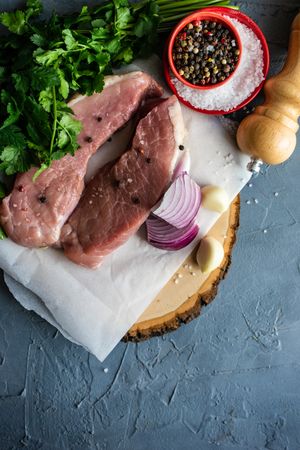 Top view of two raw pork chops with onion, garlic and herbs on kitchen counter