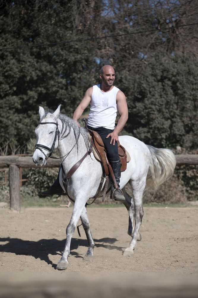 Man in sleeveless shirt riding horse on sandy ground