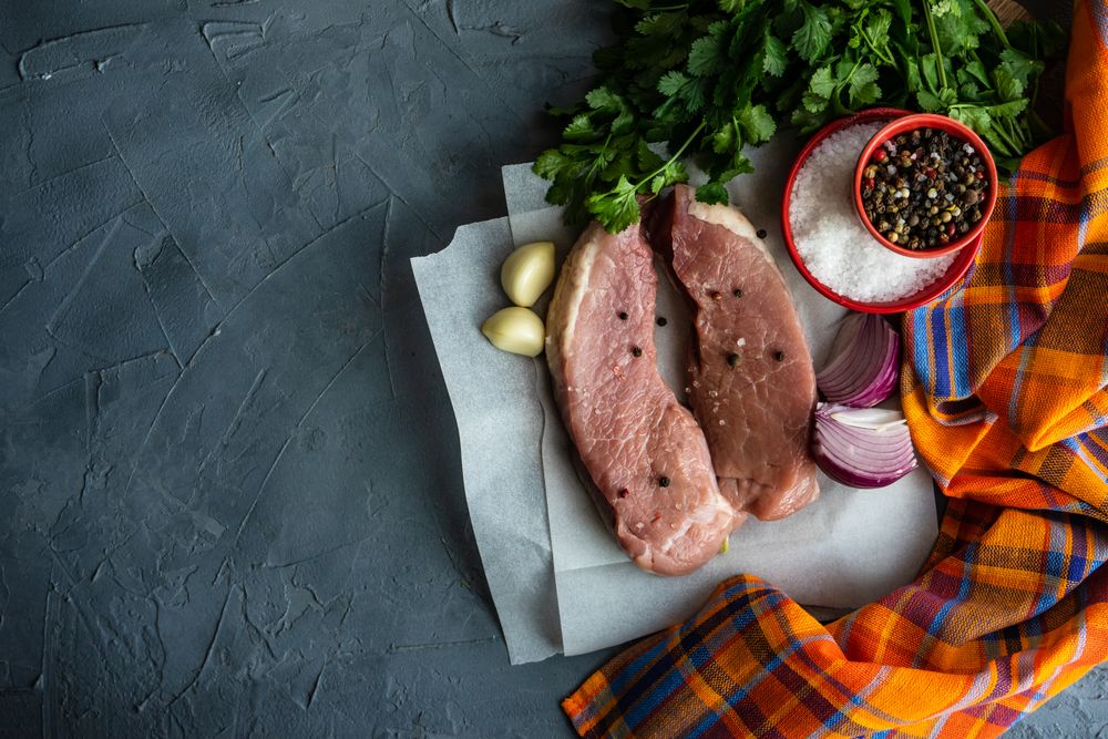 Top view of two raw pork chops with onion, garlic and herbs with copy space