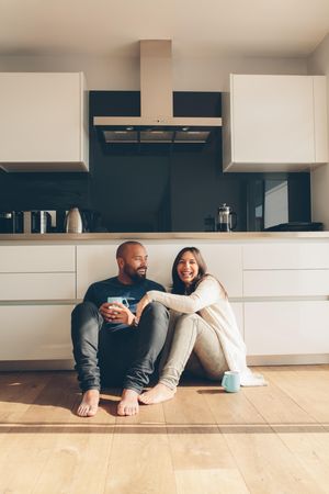 Happy young man and woman sitting on kitchen floor and having coffee