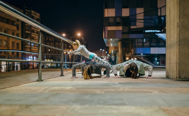 Women's sporting team doing push ups during training in the city at night