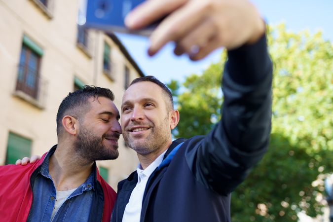 Two men taking selfie beside a building and tree