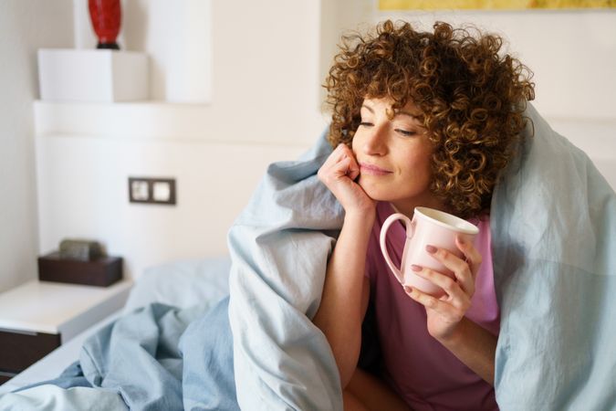 Relaxed female holding cup of hot drink on bed