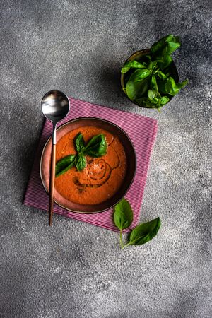 Top view of tomato soup with oil garnish and basil leaves