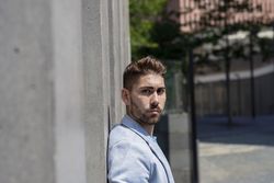 Side view of man leaning on wall outside looking at the camera