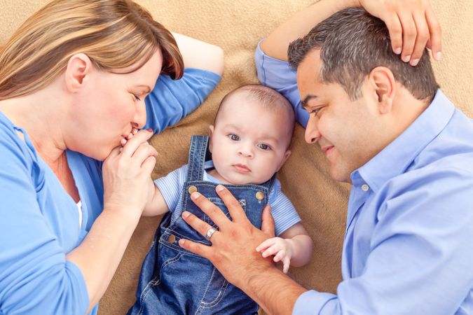 Young Couple Laying With Their Infant On A Blanket