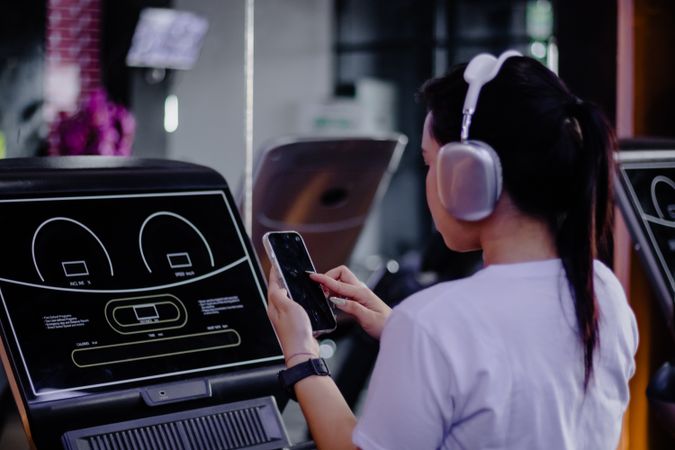 Asian woman using cellphone on treadmill for workout routine at gym