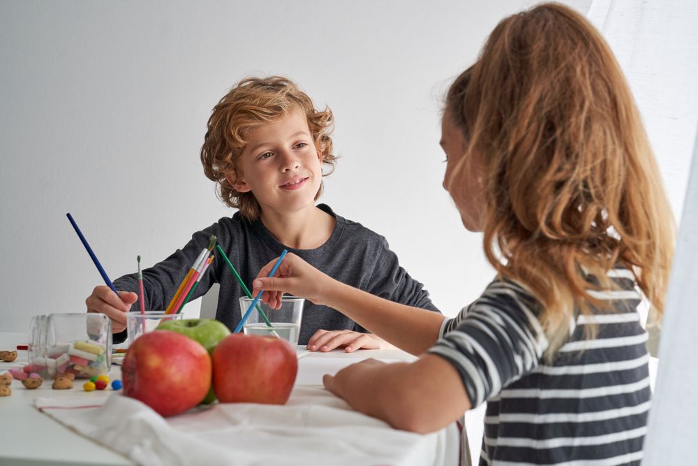 Boy painting near girl at table