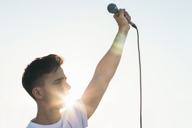 singer with the arm raised holding a microphone with sunlight reflects
