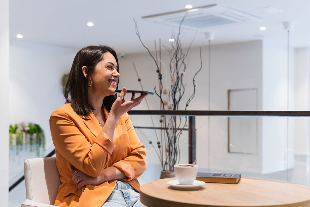 Delighted woman recording audio message on smartphone