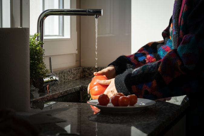 Crop woman washing tomato over sink