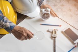 Person at work desk with hard hat, pencils, phone, clock, magnifying glass and calipers