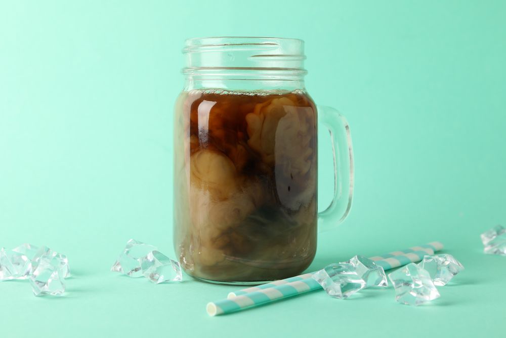 Jar of ice coffee, ice cubes and straws on mint background