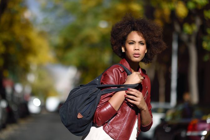 Woman looking in the distance in red leather jacket standing in sunny road
