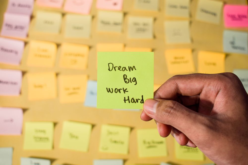 Hand hold sticky notes with words Dream Big, Work Hard