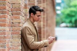 Side view of young man in camel coat texting on cell phone