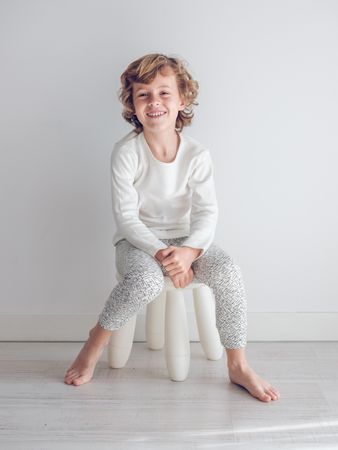 Boy in white pajamas leaning against the white wall of his house.